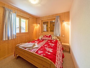 Ein Zimmer mit Holzboden, einem Bett, zwei mit Vorhängen versehenen Fenstern, einer Bank und einer Wandleuchte.