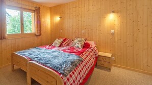 A wooden-paneled room with a bed, bedside table, and two wall-mounted lights. - Chalet Harmonie by Interhome (La Tzoumaz)