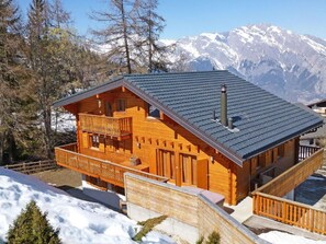 Un chalet en bois doté d’un balcon, d’une cheminée et offrant une vue sur des montagnes enneigées.