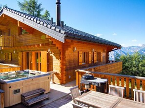 Une cabane en bois dotée d’un bain à remous et d’un espace extérieur aménagé, offrant une vue sur un paysage montagneux.