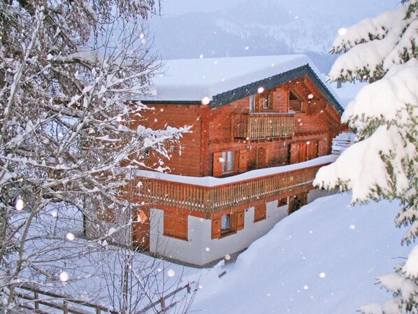 Un chalet en bois doté d’un balcon, entouré d’arbres couverts de neige.