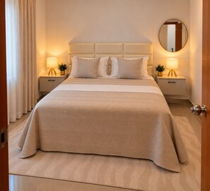 Ein Hotelzimmer mit einem großen Bett, zwei Nachttischen mit Lampen, einem runden Spiegel und einer Tür.