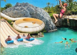 Un parc aquàtic amb un tobogan gegant, un circuit aquàtic circular i gent que gaudeix de les activitats aquàtiques.