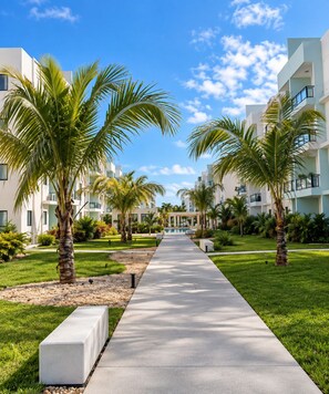 A pathway leading to a building with multiple balconies, surrounded by palm trees and greenery. - Your  Peaceful tropical  Punta Cana Getaway 2BR Condo with all amenities & more (Punta Cana)