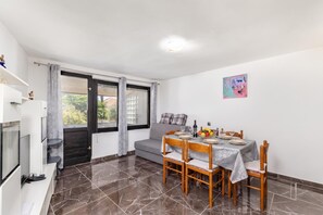 A dining area with a table set for four, a sofa, a TV, and a door leading outside. - Summer Breeze Dominique 2BR Island Retreat, Veli Iž, Croatia (Veli Iž)