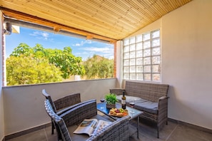 A balcony with wicker furniture, a glass table, and a bottle of wine. - Summer Breeze Dominique 2BR Island Retreat, Veli Iž, Croatia (Veli Iž)