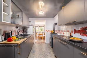 A modern kitchen with dark cabinets, a central island, and a dining area visible through an open doorway. - Summer Breeze Dominique 2BR Island Retreat, Veli Iž, Croatia (Veli Iž)
