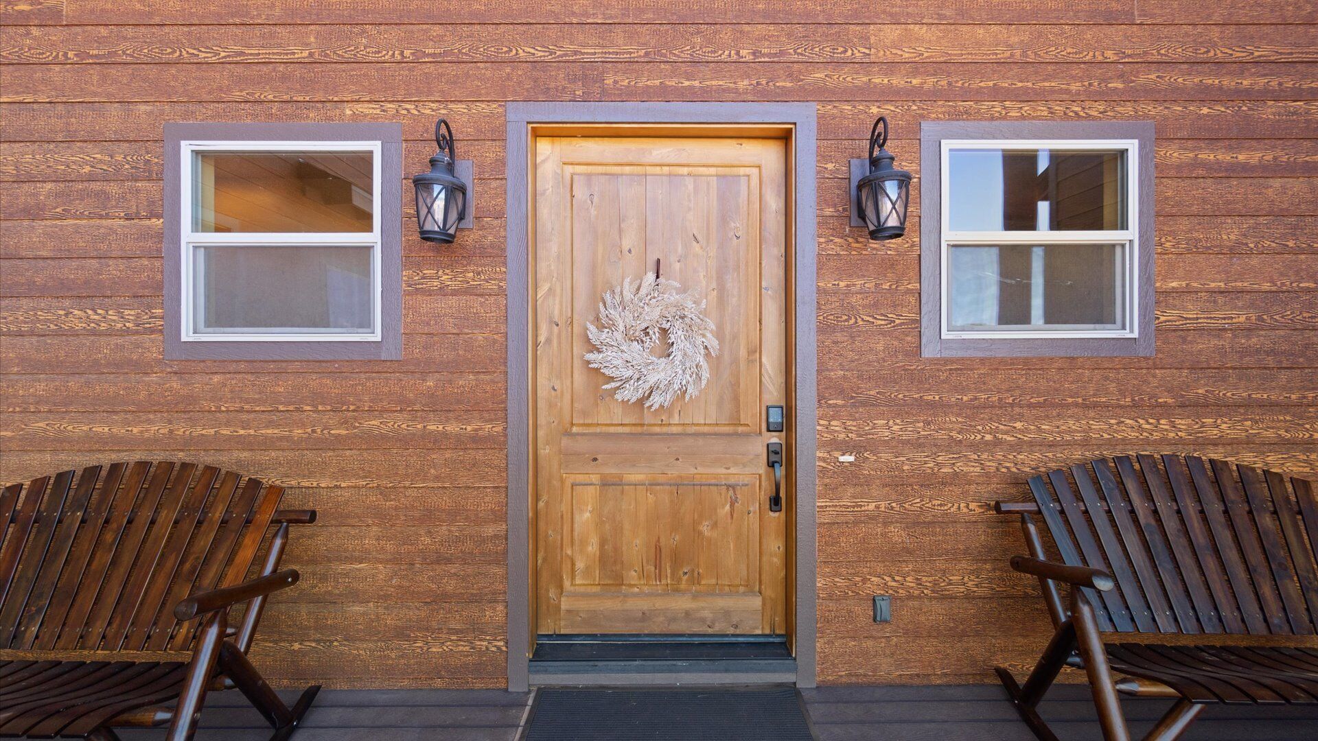 A wooden building with a central door, two windows on either side, and two rocking chairs in front.