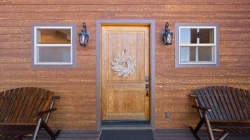 A wooden building with a central door, two windows on either side, and two rocking chairs in front.