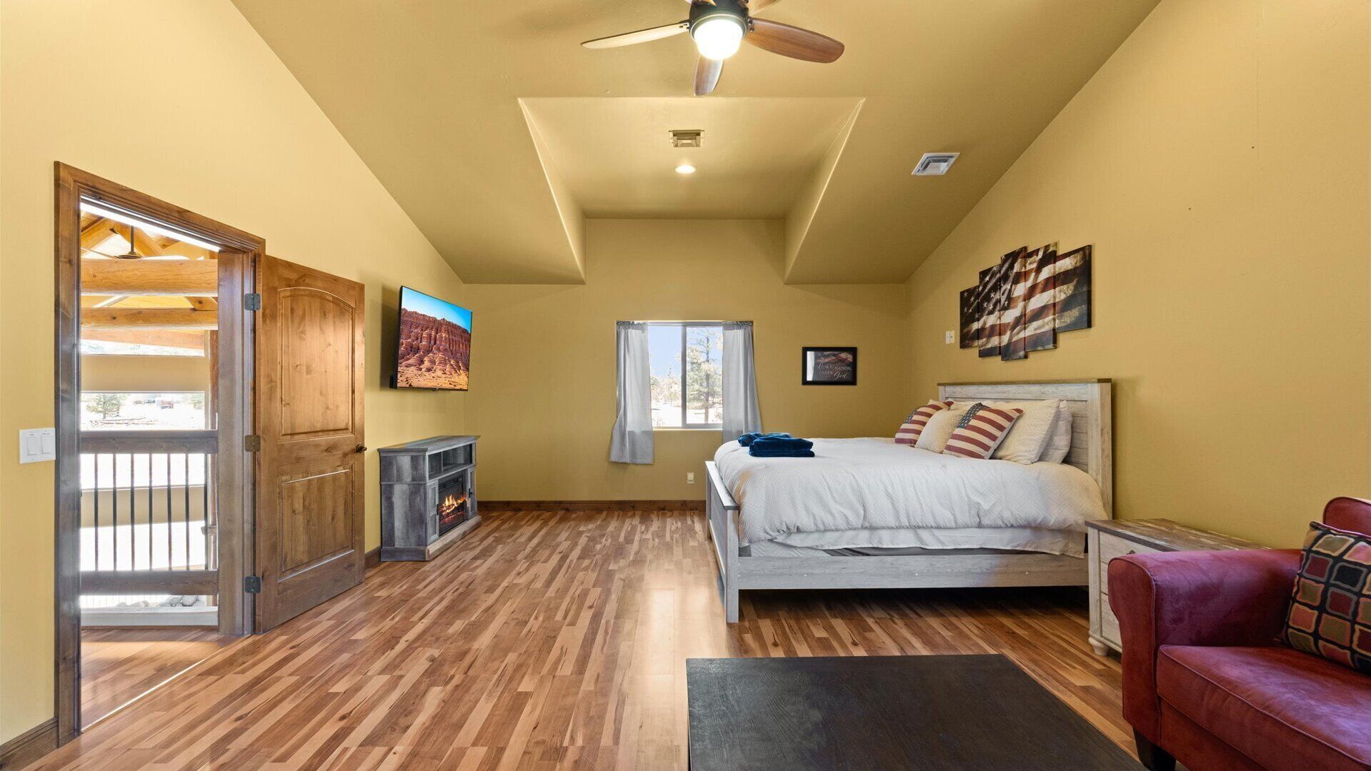 Una camera da letto con un letto, una ventola a soffitto, un camino, una finestra e una porta che dà su un balcone.
