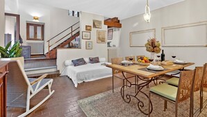Un vaste espace de vie comprenant une table à manger pour deux personnes, un canapé, un escalier et une vue sur l’extérieur.