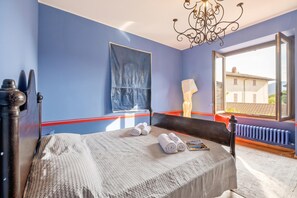 A bedroom with a bed, a window with a view, a radiator, and a chandelier. - The Place to Be, Outdoor dining, Laveno Mombello, Italy (Laveno Mombello)