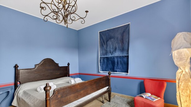 Une chambre à coucher avec un lit en bois, une chaise rouge, une fenêtre et un lustre.