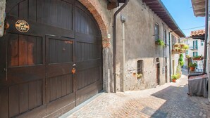 Une ruelle étroite pavée, avec une grande porte en bois et une pancarte sur laquelle on peut lire : « ATTENTION, CHIEN ».