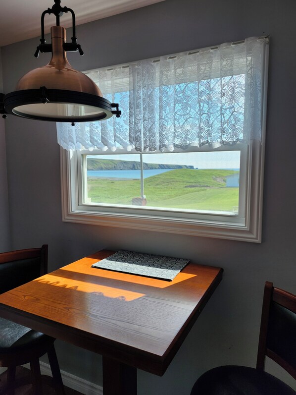 A dining area with a table, chairs, a lamp, and a window with a view of a landscape.