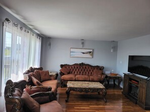 Ett vardagsrum med en brun lädersoffa, en tillhörande fåtölj, ett soffbord och en tv som står på ett träskåp.