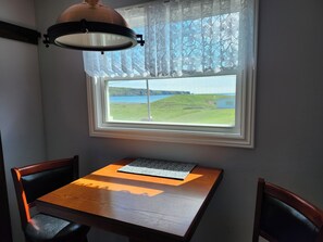 A table with a laptop, a lamp, and a view of a grassy landscape through a window.
