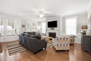 A spacious living room with a grey sofa, patterned armchairs, a flat-screen TV, and a fireplace. - Luxury 6BR 3 BA Beach Home Sleeps 14 Huge Front Porch Walk To Beach and Downtown (Ocean City)