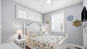 A bedroom with a bed, nightstand, lamp, and wall decorations. - Luxury 6BR 3 BA Beach Home Sleeps 14 Huge Front Porch Walk To Beach and Downtown (Ocean City)