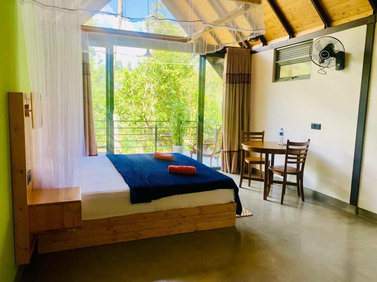 Um quarto com uma cama, uma mesa, cadeiras, um ventilador e uma janela com cortinas.