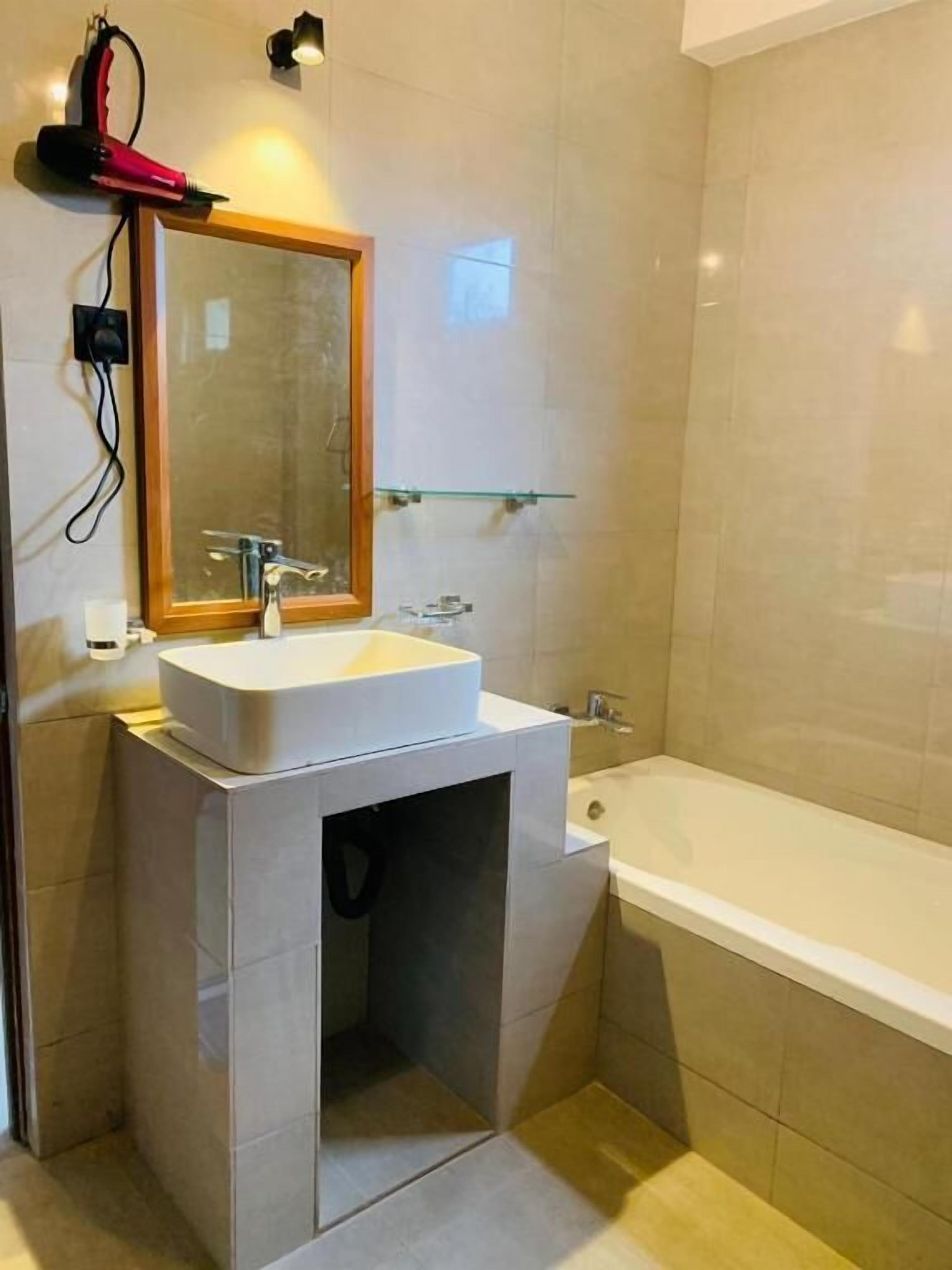 Un baño con lavamanos blanco, espejo, repisa de vidrio y bañera.