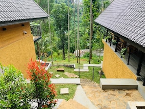 A courtyard with a stone pathway, a small garden area, and two buildings with tiled roofs. - Happy Sky Ella (Ella)