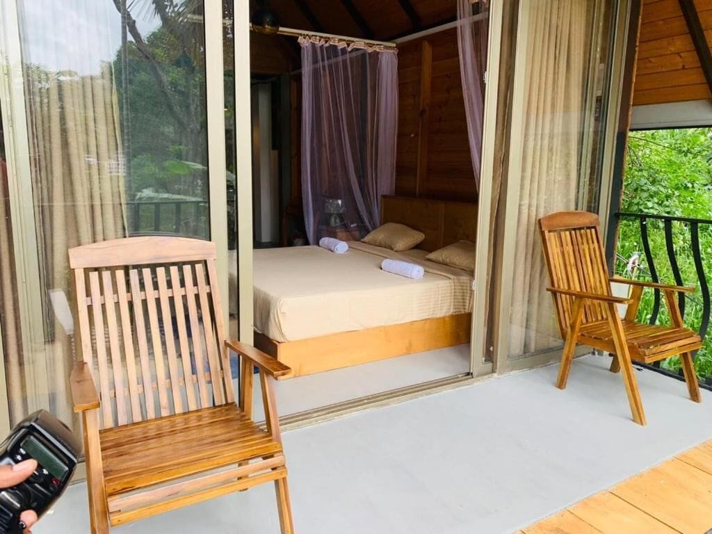 Una habitación con una cama, dos sillas de madera y un separador de vidrio.