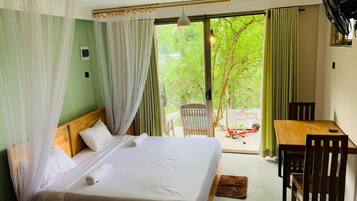 Une chambre avec un lit, une table, des chaises, un ventilateur et une vue sur la verdure.