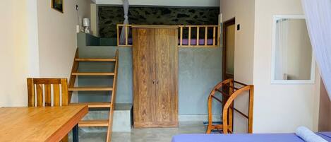 A room with a wooden desk, a bed with a blue bedspread, a wooden wardrobe, and a staircase.