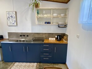 Ett kök med en stor diskho, skåp, en bänkskiva med en vattenkokare och en hylla med glasvaror.