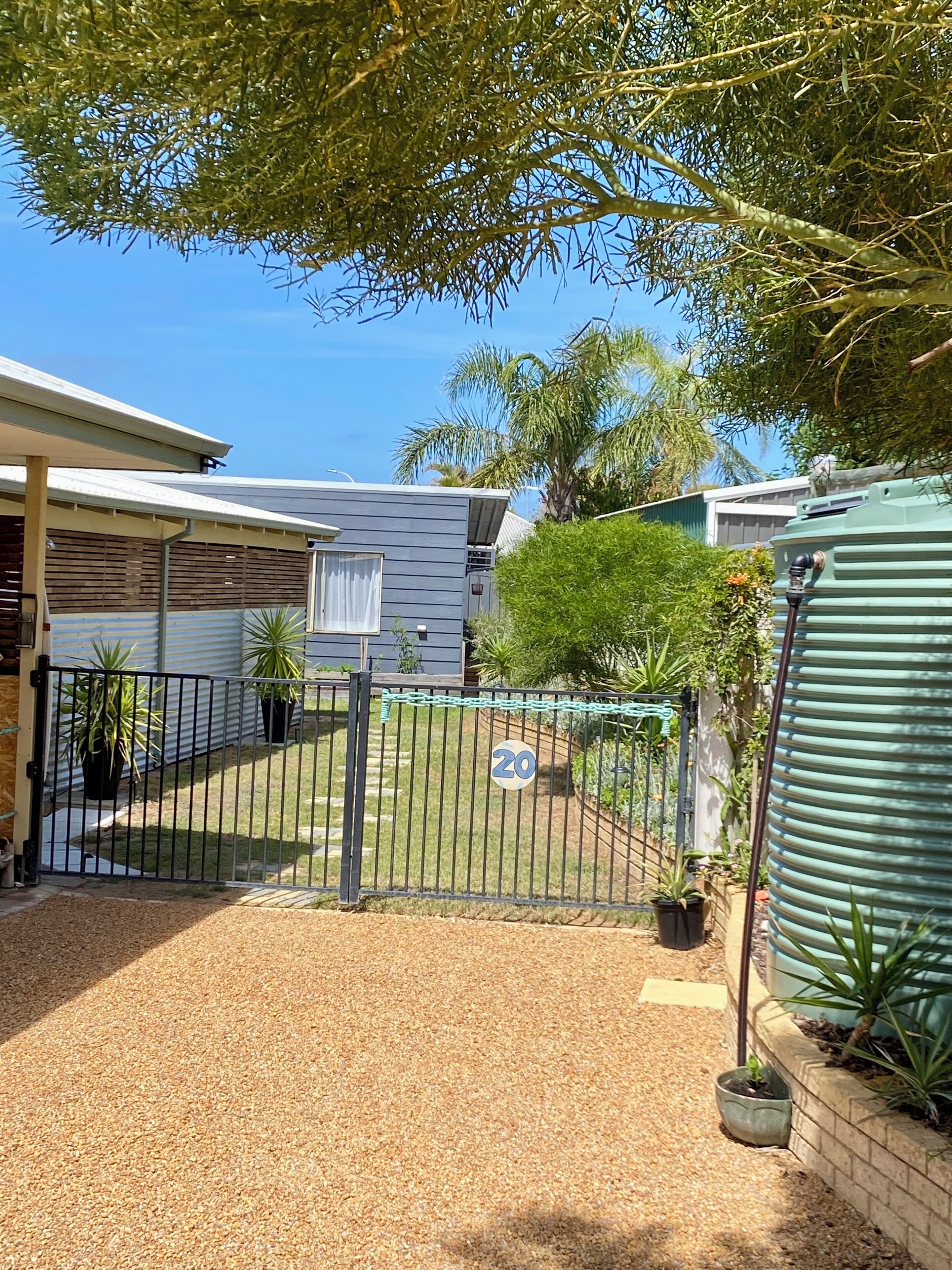 A fenced backyard with a gravel path, a gate, and potted plants.