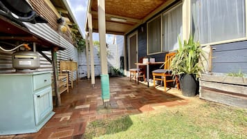 Ein überdachter Patio-Bereich mit Ziegelboden, Holzmöbeln und einem Blumentopf.