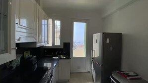 Eine kleine Küche mit weißen Schränken, einer schwarzen Arbeitsplatte, einem Kühlschrank und einem Fenster mit Blick.