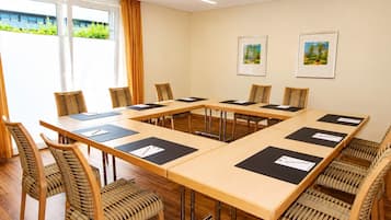 Un salón de conferencias con una larga mesa, sillas y dos cuadros en la pared.