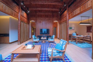 A spacious living room with a large flat-screen TV, wooden furniture, and a patterned floor.