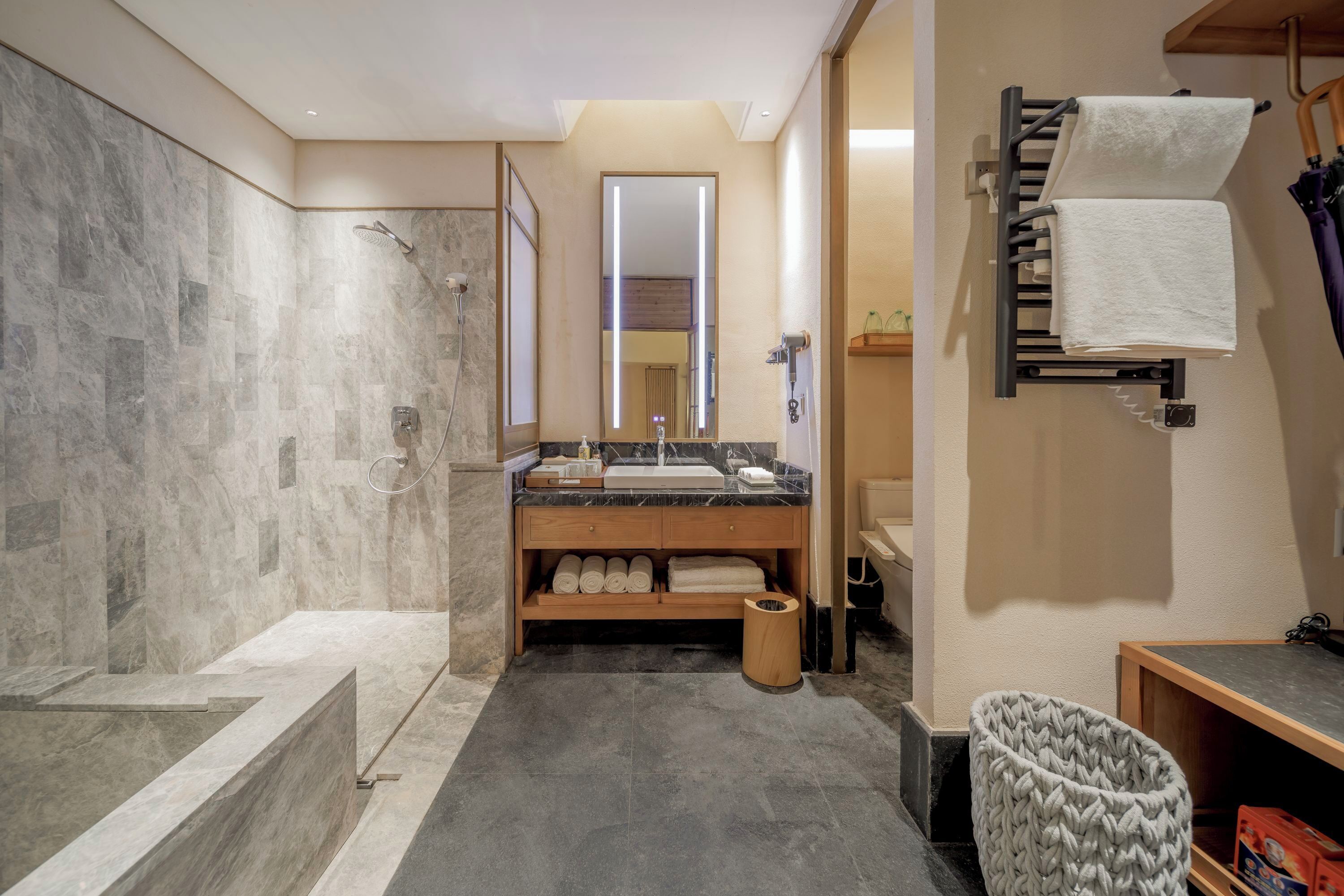 Un baño moderno con ducha de mármol, lavamanos con toallero y tocador de madera.