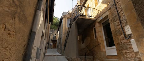 Un estrecho callejón flanqueado por edificios de piedra, una escalera y una barandilla metálica.