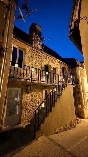 A stone building with a staircase leading to a balcony, under a twilight sky. - Hostcare - Le Secret Sarladais – Downtown (Sarlat-la-Canéda)
