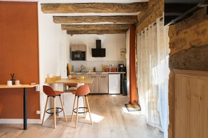 A modern kitchen with wooden beams, a dining area with two chairs, and a kitchen island. - Hostcare - Le Secret Sarladais – Downtown (Sarlat-la-Canéda)
