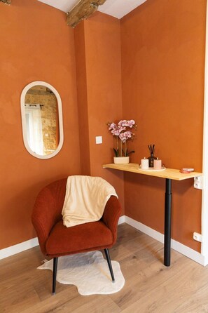 A room with a red chair, a small table with a potted plant, and a mirror on the wall. - Hostcare - Le Secret Sarladais – Downtown (Sarlat-la-Canéda)