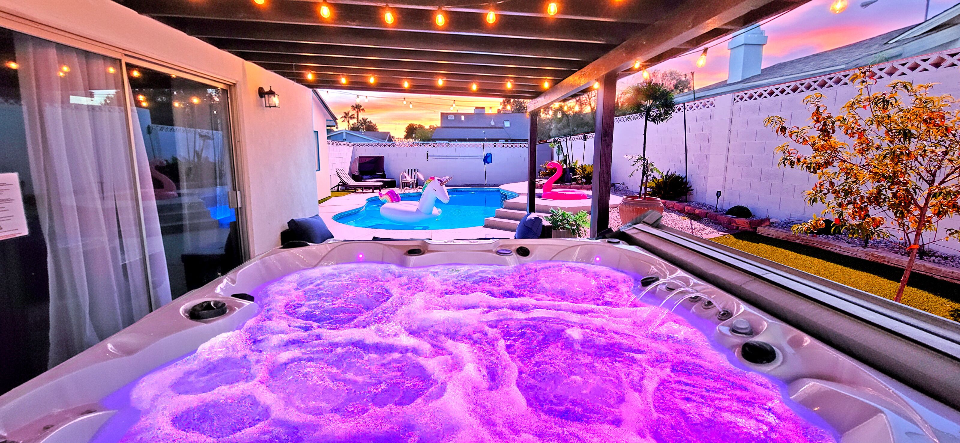 A hot tub with a unicorn float, a pool, and a patio area with string lights.
