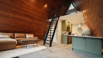 A loft-style room with a wooden ceiling, a sofa, a ladder, and a kitchenette.