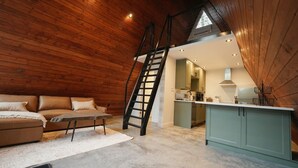 Un habitación estilo loft con techo de madera, una cama en alto, kitchenette y zona de comedor.