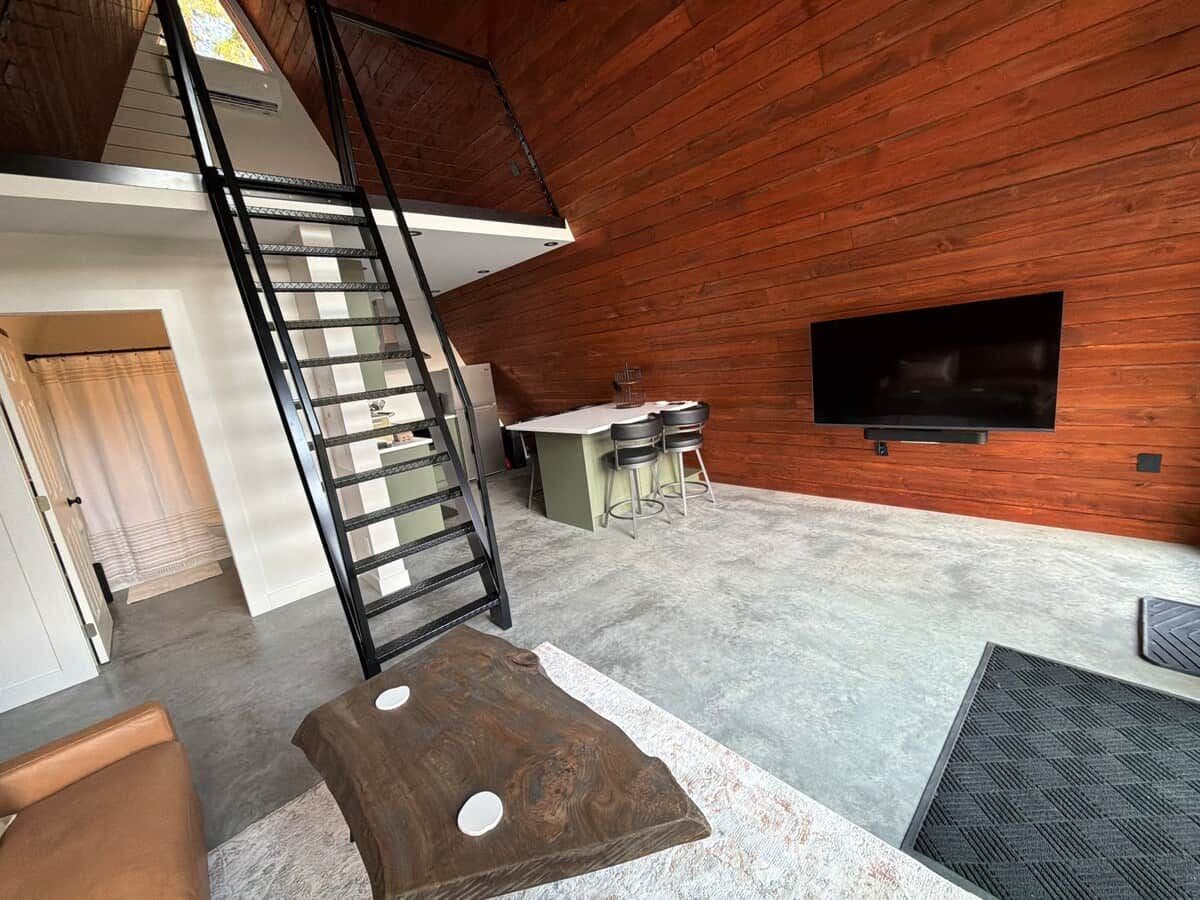Interior moderno com parede de madeira, escada, área de cozinha e televisão de tela plana.