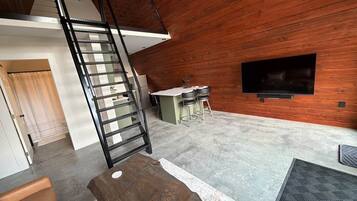 Interior moderno com parede de madeira, escada, área de cozinha e televisão de tela plana.