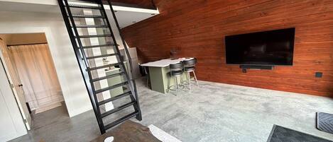 A modern interior with a wooden wall, a staircase, a kitchen area, and a flat-screen TV.