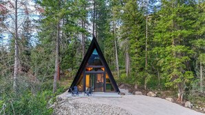Una cabaña moderna de forma triangular con fachada de vidrio, rodeada de un bosque denso.
