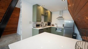 Una cocina moderna con armarios verdes, encimeras blancas y electrodomésticos de acero inoxidable.