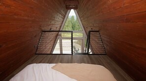 A room with a bed, a window with a view of trees, and a wooden ceiling.