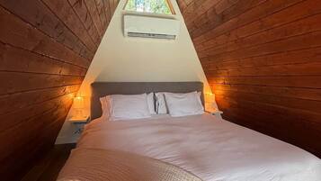 Quarto triangular com cama, duas luminárias de apoio e uma janela.